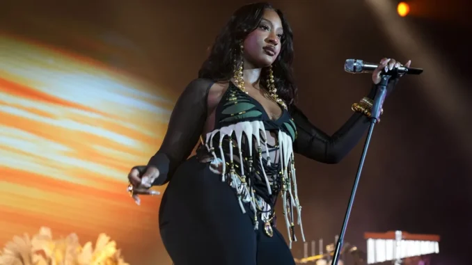 tems-in-a-bold-stage-outfit-sings-into-a-microphone-during-a-live-concert-under-dramatic-lighting